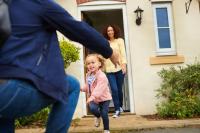 Child running to father with mother standing and smiling in the house doorway behind the child.